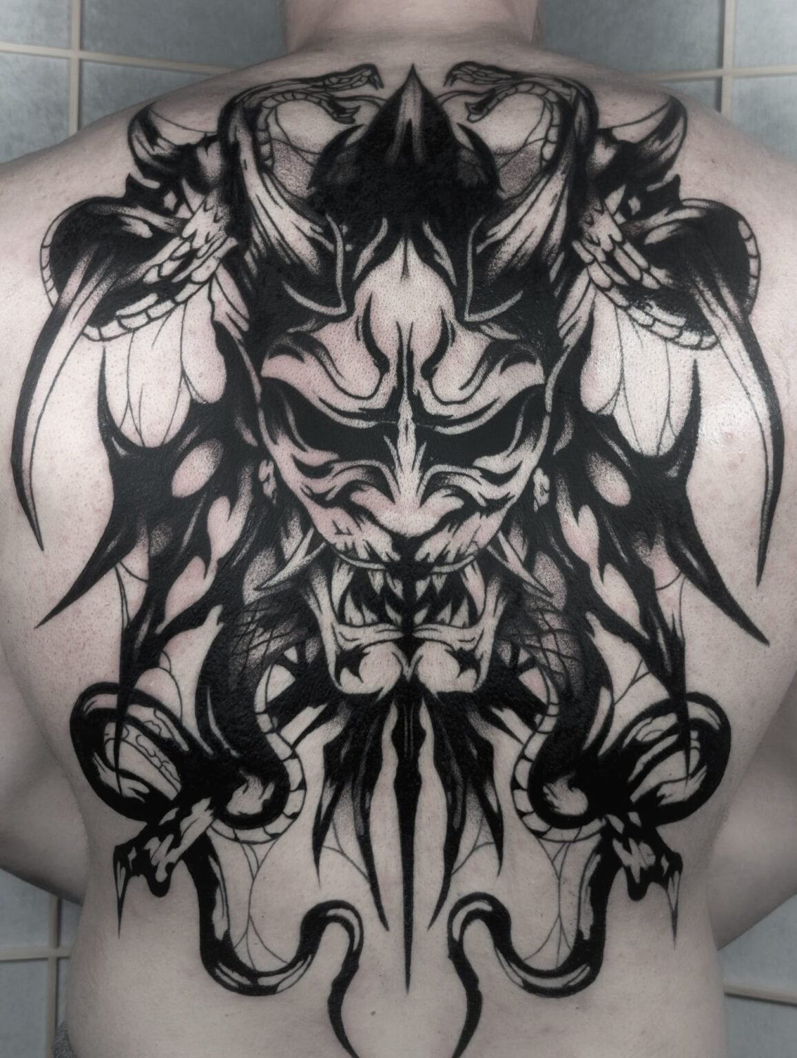 Großflächiges Rücken-Tattoo mit dämonischer Oni-Maske und Schlangen – kraftvolles Blackwork. Exklusive Tattoos aus Menden, Unna, Wickede, Iserlohn, Werl.