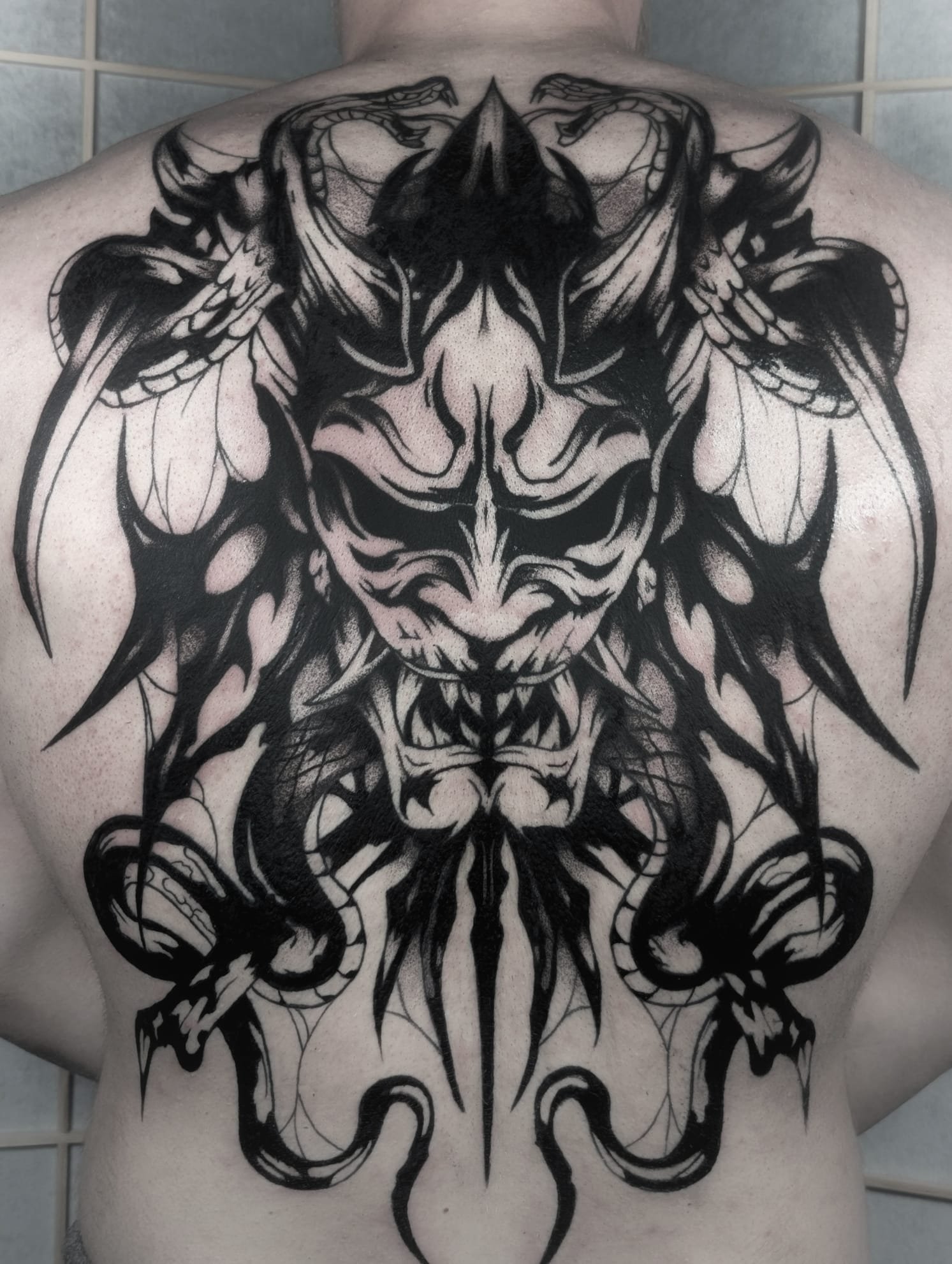 Großflächiges Rücken-Tattoo mit dämonischer Oni-Maske und Schlangen – kraftvolles Blackwork. Exklusive Tattoos aus Menden, Unna, Wickede, Iserlohn, Werl.